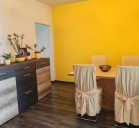 A dining room with a wood-patterned floor and a yellow wall in a three-room apartment.