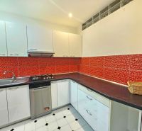 A kitchen with white cabinets, red tiles, and stainless steel appliances in a three-room apartment.