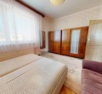 A bedroom in a family house with a bed, cabinets, and a chair, floral wallpaper on the walls.