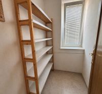 Narrow room in a family house with a shelving unit and a window with blinds.