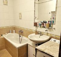 A bathroom in a 3-room apartment with a bathtub, a sink, and a mirror full of cosmetics.