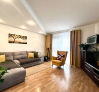 Living room in a three-room apartment with a corner sofa, wooden decor flooring, and a yellow armchair.
