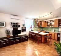 A kitchen in a 3-room apartment with an island, wooden decor flooring, and an open space.