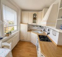 A kitchen in a 3-room apartment with a wooden decor floor and white furniture.