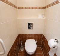 A toilet in a 3-room apartment with light tiles and a storage shelf.