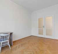 A room in a 3-bedroom apartment with a desk, a white chair, and a floor with a wooden decor.