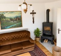 Living room in a family house with a brown couch, a tile stove, and a landscape painting.