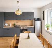 A kitchen in a family house with a wooden decor and dark gray kitchen cabinets, light streaming through the window.