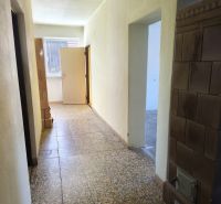 A hallway in a family house with a tiled stove and a window at the end.