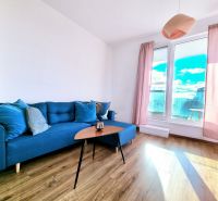 A blue sofa in the living room with light curtains and a wood-patterned floor.