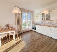 A kitchen in a two-room apartment with a wooden decor floor and white cabinets.