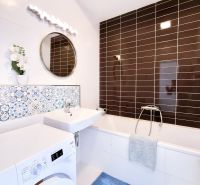 Bathroom in a 2-room apartment with a washing machine, bathtub, sink, and decorative tiles.