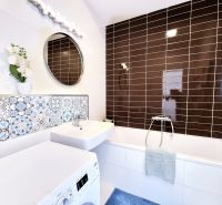 Bathroom in a 2-room apartment with white and brown tiles, with a sink and a washing machine.