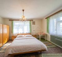 A bedroom in a family house with a wardrobe, bed, and chandelier, illuminated by natural light.