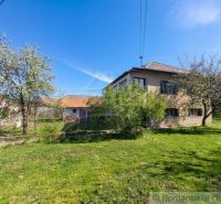 A family house in Kriváň surrounded by fruit trees and a manicured lawn under a clear sky.