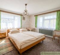 Bedroom in a family house with a bed, carpet, and large windows with green curtains.