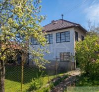 A family house in Kriváň with a front garden, a blooming tree, and a blue sky.