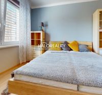 A bright bedroom in a two-room apartment with wood-patterned flooring and a large window.