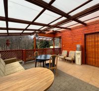 Covered terrace of the cottage in Svinica with seating and a forest view.