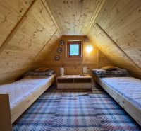 An attic room in a cottage with two beds and wooden decor.