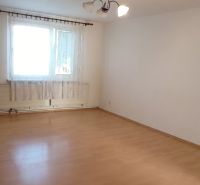A room with a wooden decor floor in a 3-room apartment, light walls, and a window with a curtain.