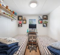 A children's room in a cottage with beds and toys on shelves, with a wooden decor floor.
