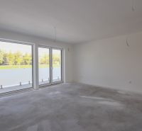 Empty room with large windows in a 2-room apartment and a view of a green area.