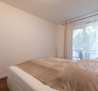 Bedroom with a bed and a window, floor with wooden decor, light curtains in a 2-room apartment.