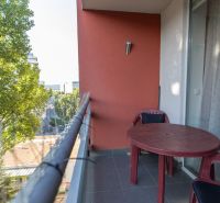 A balcony of a 2-room apartment with plastic furniture and a view of greenery.