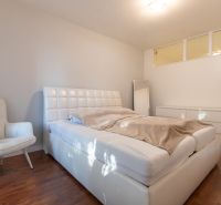 A bedroom with a white bed, an armchair, and a wooden decor floor.