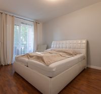 A bedroom in a 2-room apartment with a white bed and a wooden decor floor.