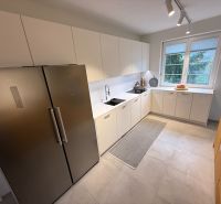 A kitchen in a family house with white cabinets, a stainless steel refrigerator, and a window with a view.