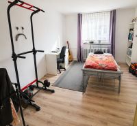 A bedroom with wood-patterned flooring, exercise equipment, and a work desk in a family house.