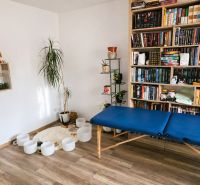 A room in a family house with a wooden decor floor, a bookshelf, and a massage table.