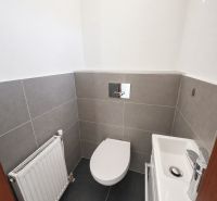 A toilet with a sink in a family house, with gray tiles on the walls and floor.