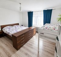A bedroom in a family house with a bed, a bunk bed, and a wooden decor floor.