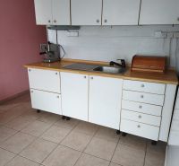 A kitchen in a 2-room apartment with white cabinets, tiles, and a coffee maker.