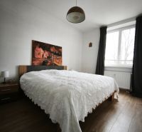 A bedroom with a bed, painting, wood-patterned floor, and curtains in a 4-room apartment.