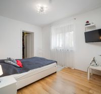 A bright bedroom with wood-decor flooring, a bed, and a TV on the wall in a family house.