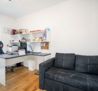 An office in a family house with a black sofa, a desk, and a wooden decor floor.