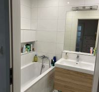 A bathroom in a 3-room apartment with a bathtub, a sink, and a floor with a wooden decor.