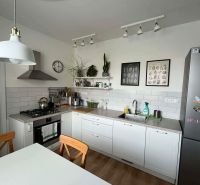 A kitchen in a 3-room apartment with white cabinets, a wooden decor floor, and decorations.