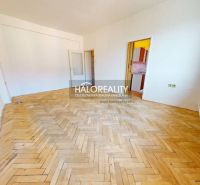 A room in a 2-room apartment with a large floor with wooden decor, white walls, and a window.
