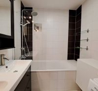 A white bathroom with a bathtub, black tiles, and a shower in a 3-room apartment.