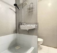 A bathroom in a studio apartment with white tiles and a shower corner.