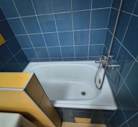 A bathroom with blue and yellow tiles and a bathtub in a studio apartment.