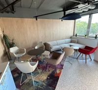 A comfortable office with modern furniture and large windows, carpeted floor.