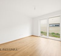 A spacious room with a wood-patterned floor and a large window in a family house.