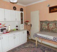 A kitchen in a family house with white cabinets, a microwave, and a table with a tablecloth.