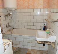 A bathroom with older fixtures, tiles, and a bathtub in a family house.